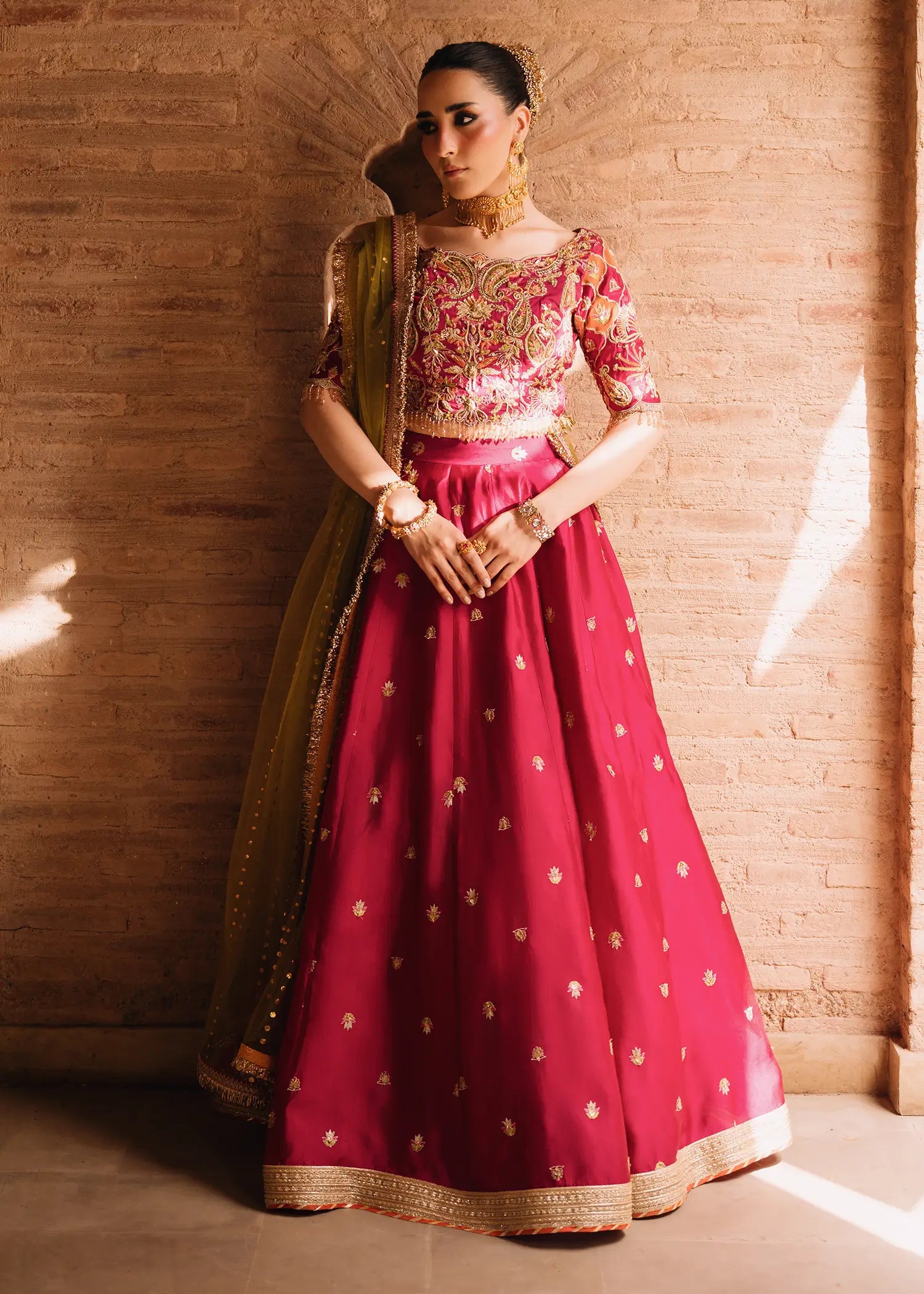 Fuschia Anaya magenta lehnga choli with traditional resham and gota embroidery paired with a contrasting olive-green dupatta for festive elegance.